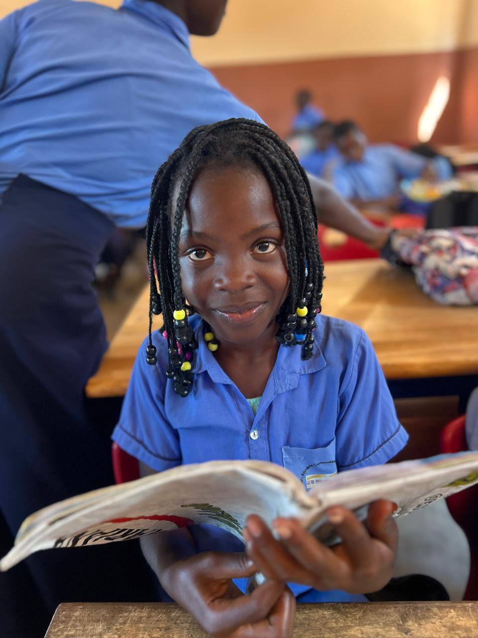A student in an ASEM school uniform smiles while reading a book in class.